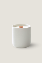 A minimalist white ceramic candle jar labeled 'LUCERIA' with a single wick on top, set against a solid light beige background. Luceria's Oakmoss and White Cedar Candle.