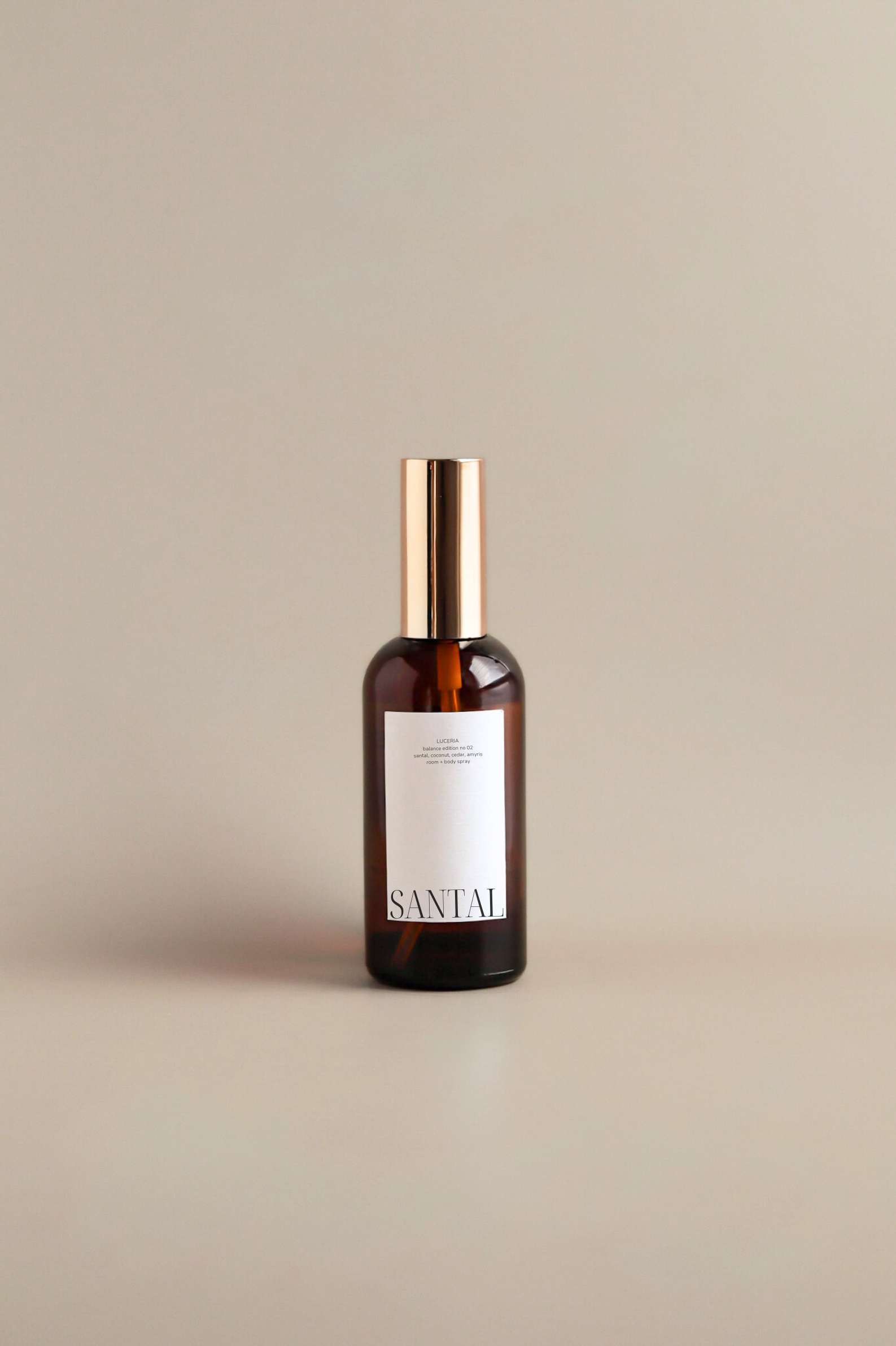 Bottle of Santal coconut spray with a gold cap on a beige background