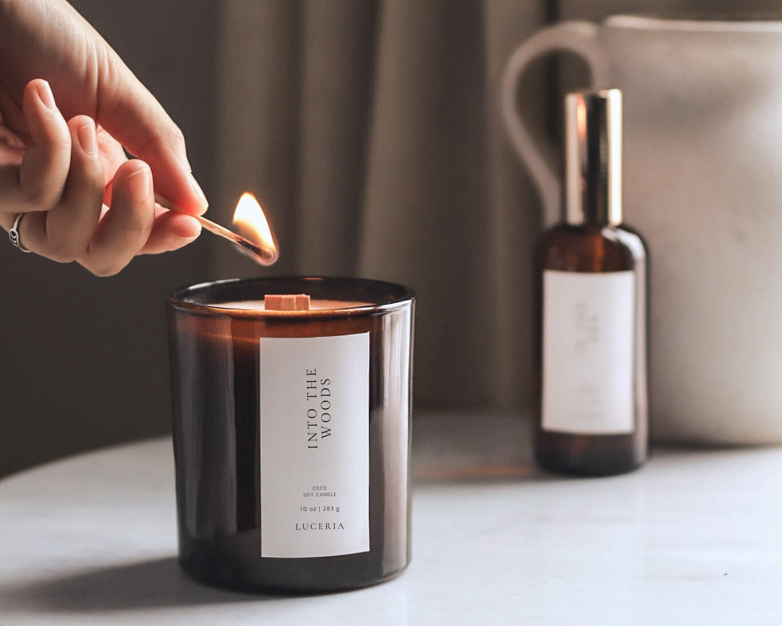 Person lighting the gentle reset candle with a match on a table next to a bottle and a bag.