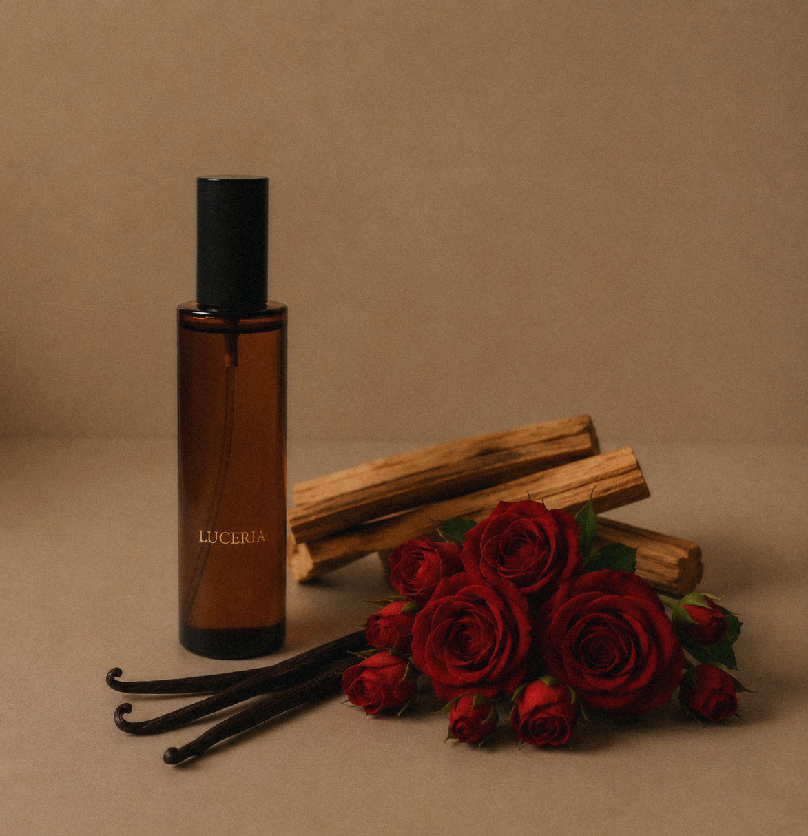 Veil room and linen spray amber glass bottle with a black cap stands on a beige surface, styled with red roses, vanilla beans, and wood pieces against a matching beige background. The bottle is labeled LUCERIA.
