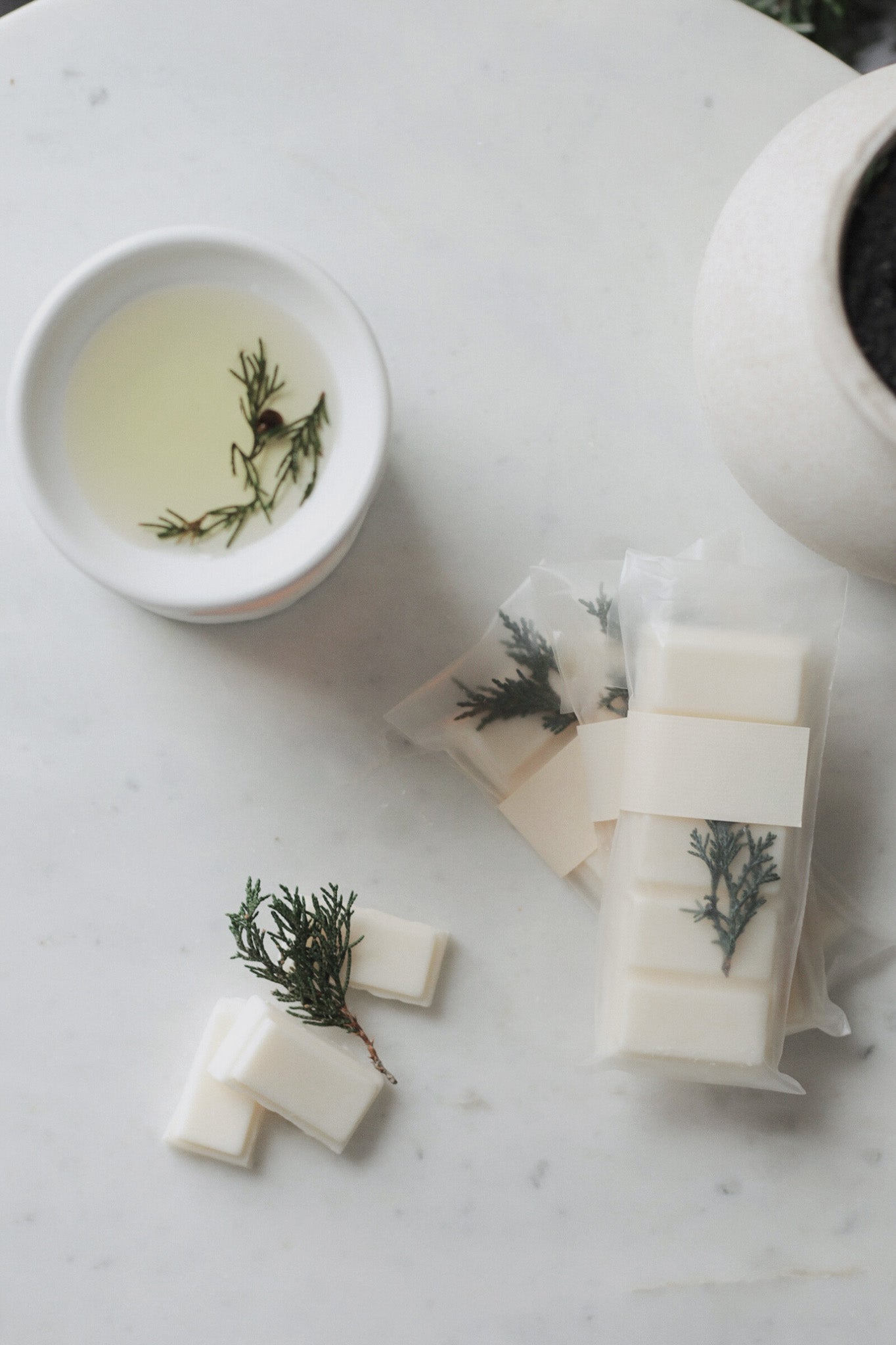 wax melt bars with greenery on a marble surface next to a small bowl of liquid.