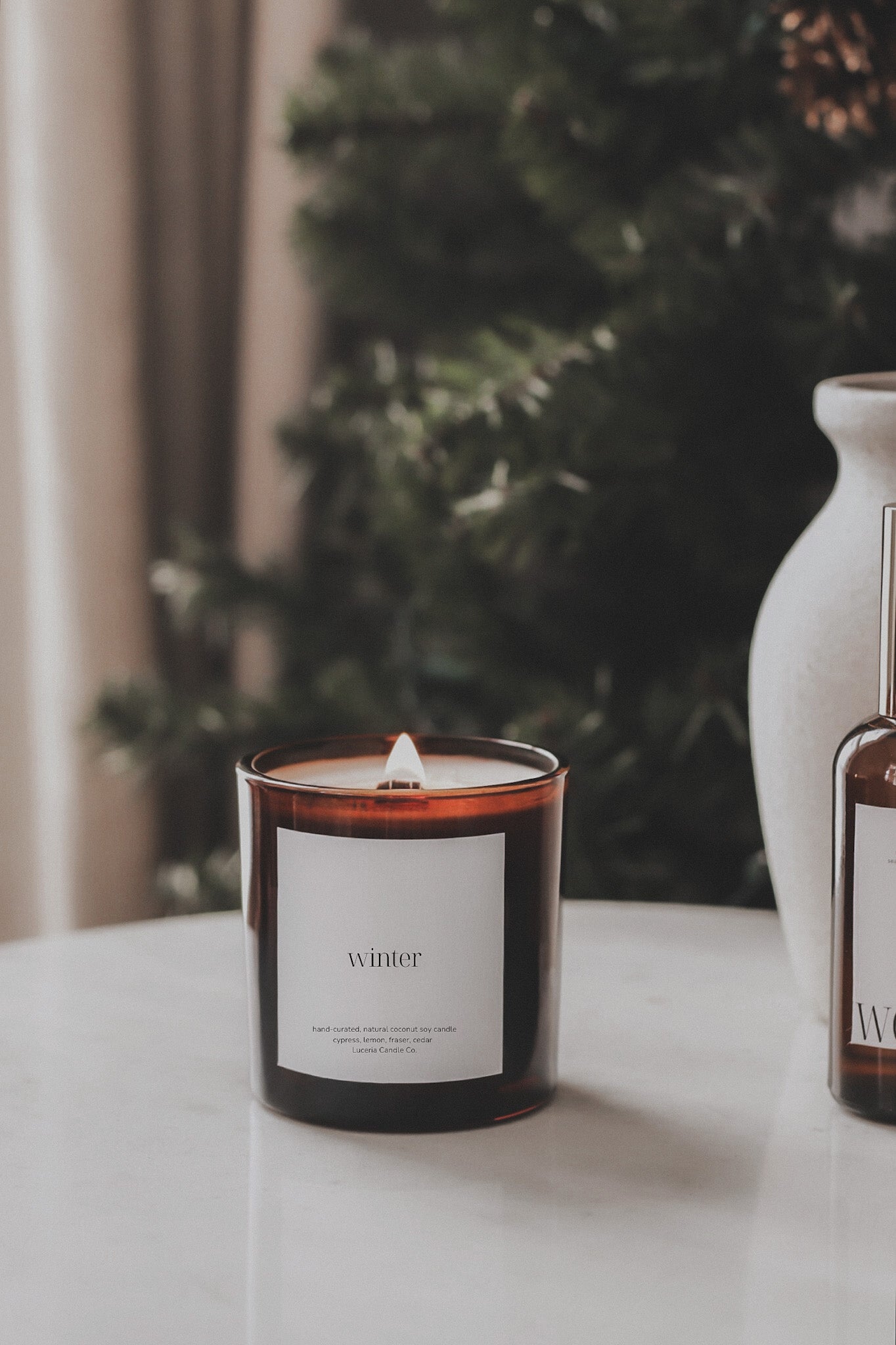 Candle labeled 'winter' on a table with a blurred Christmas tree in the background