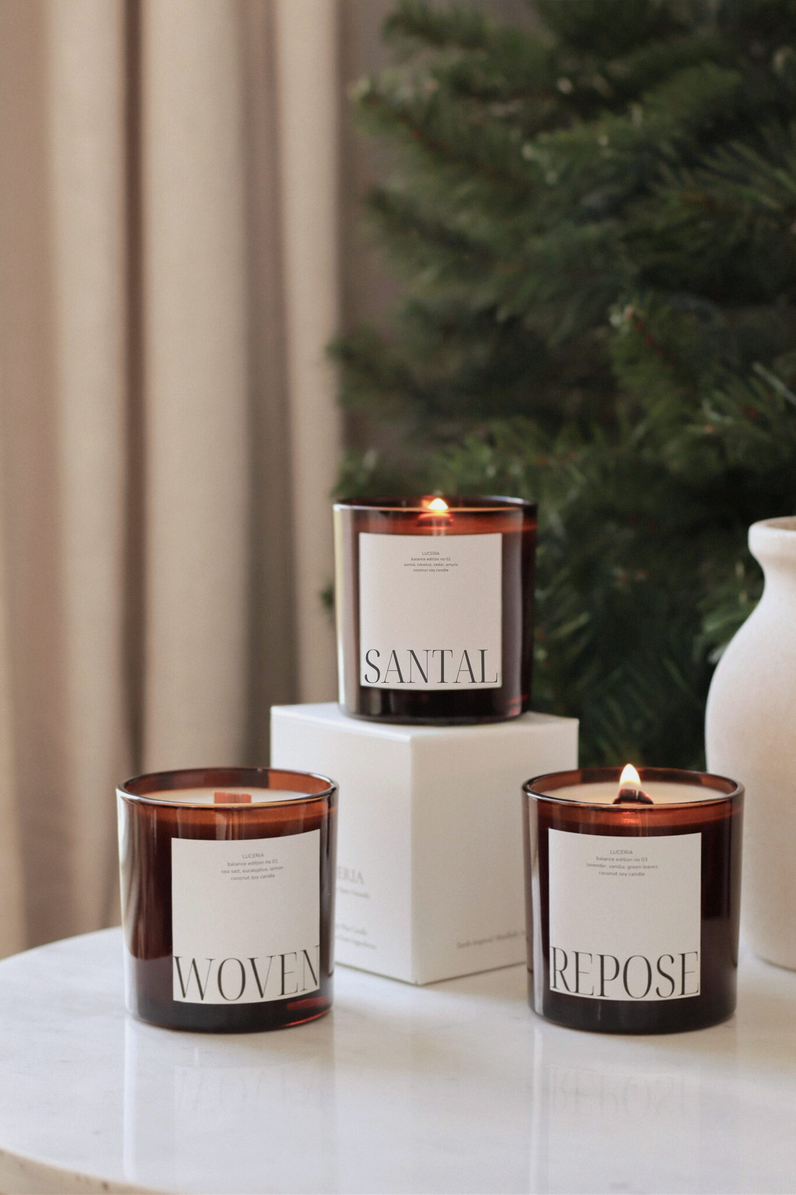 Three scented candles labeled 'Woven', 'Santal', and 'Repose' on a surface with a blurred background.