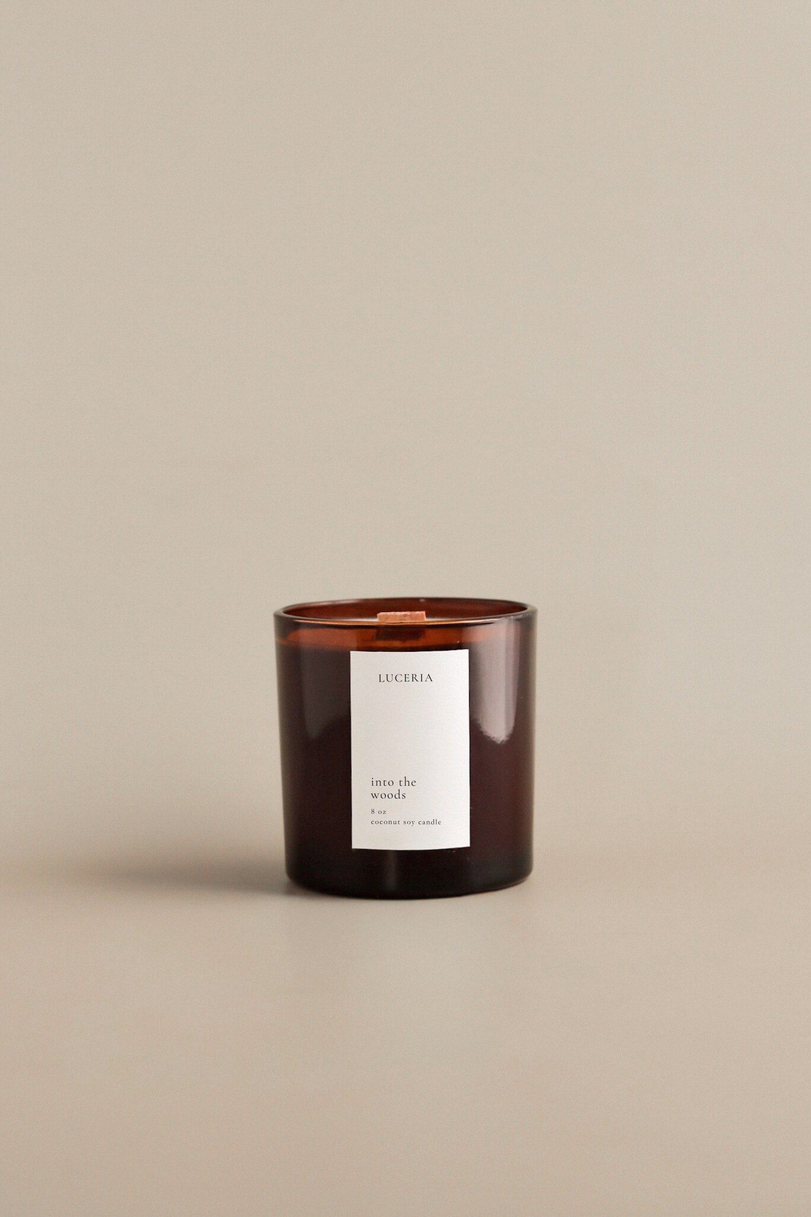 Brown amber candle with Into the Woods label on a beige background by Luceria