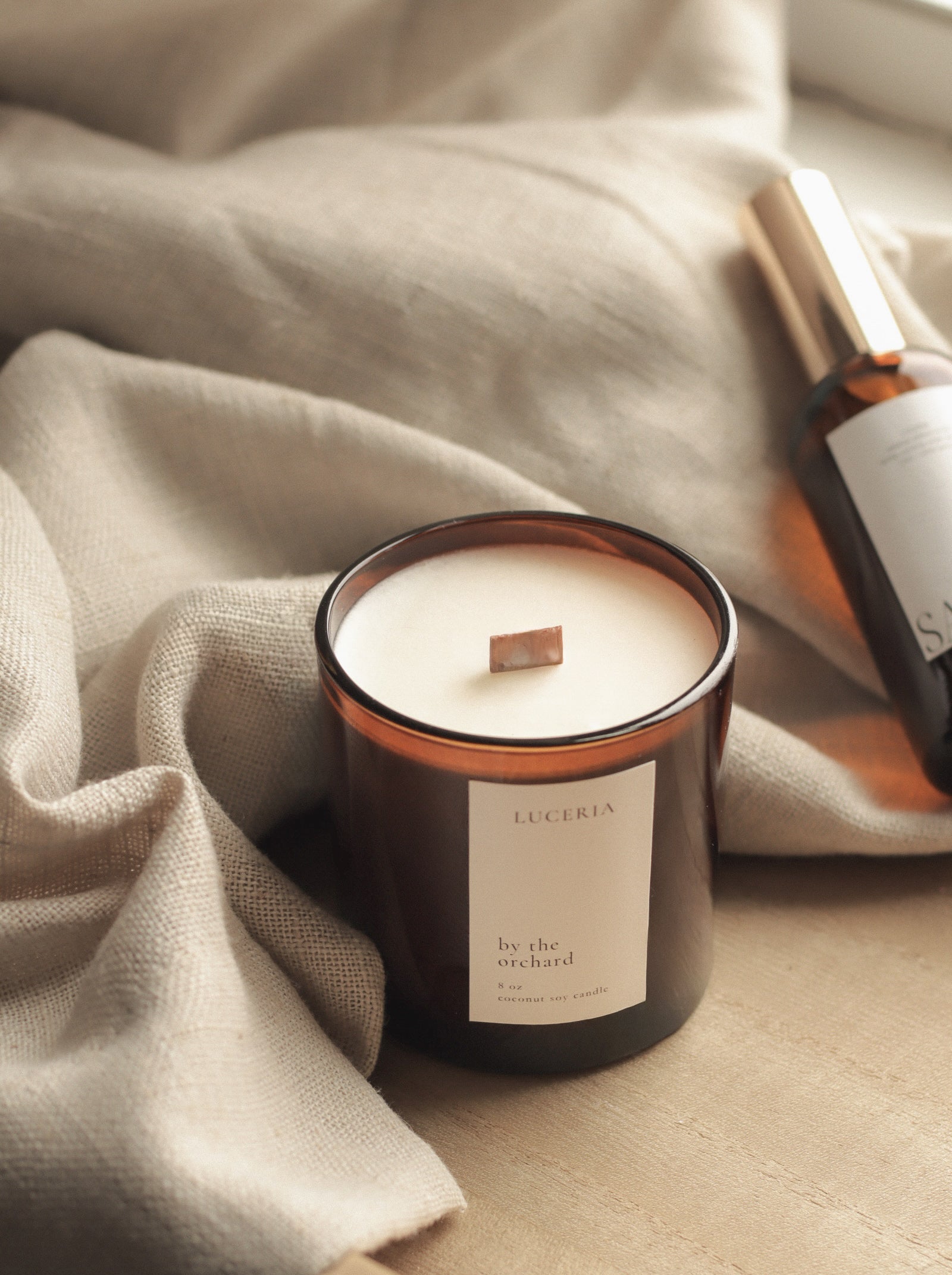 Candle with a label on a textured surface next to a bottle of perfume.