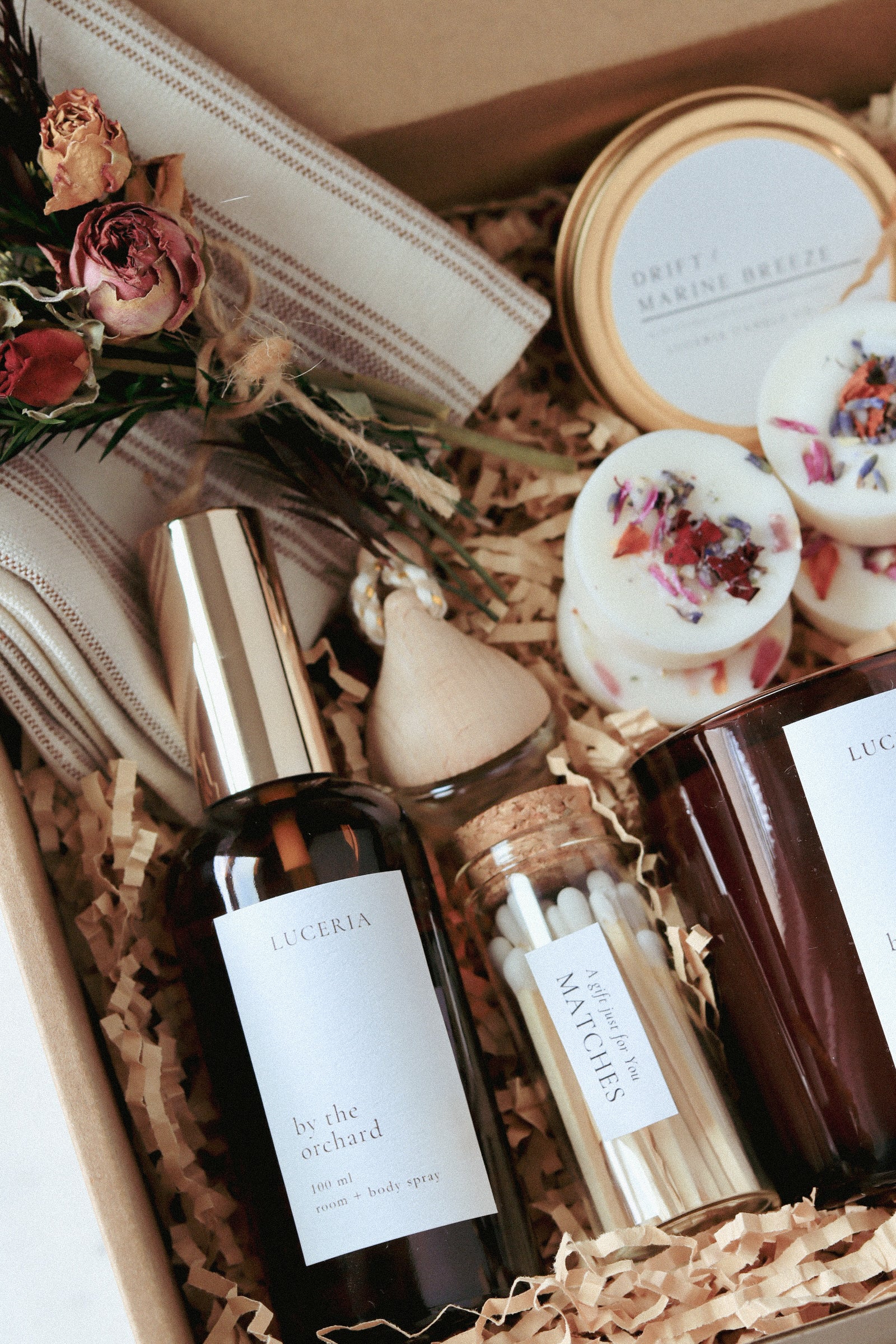 Gifting box with body products, bath bombs, and flowers in a kart box with Kraft shredded paper.