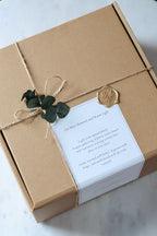 Gift box wrapped in brown paper with a white card and greenery on a light background