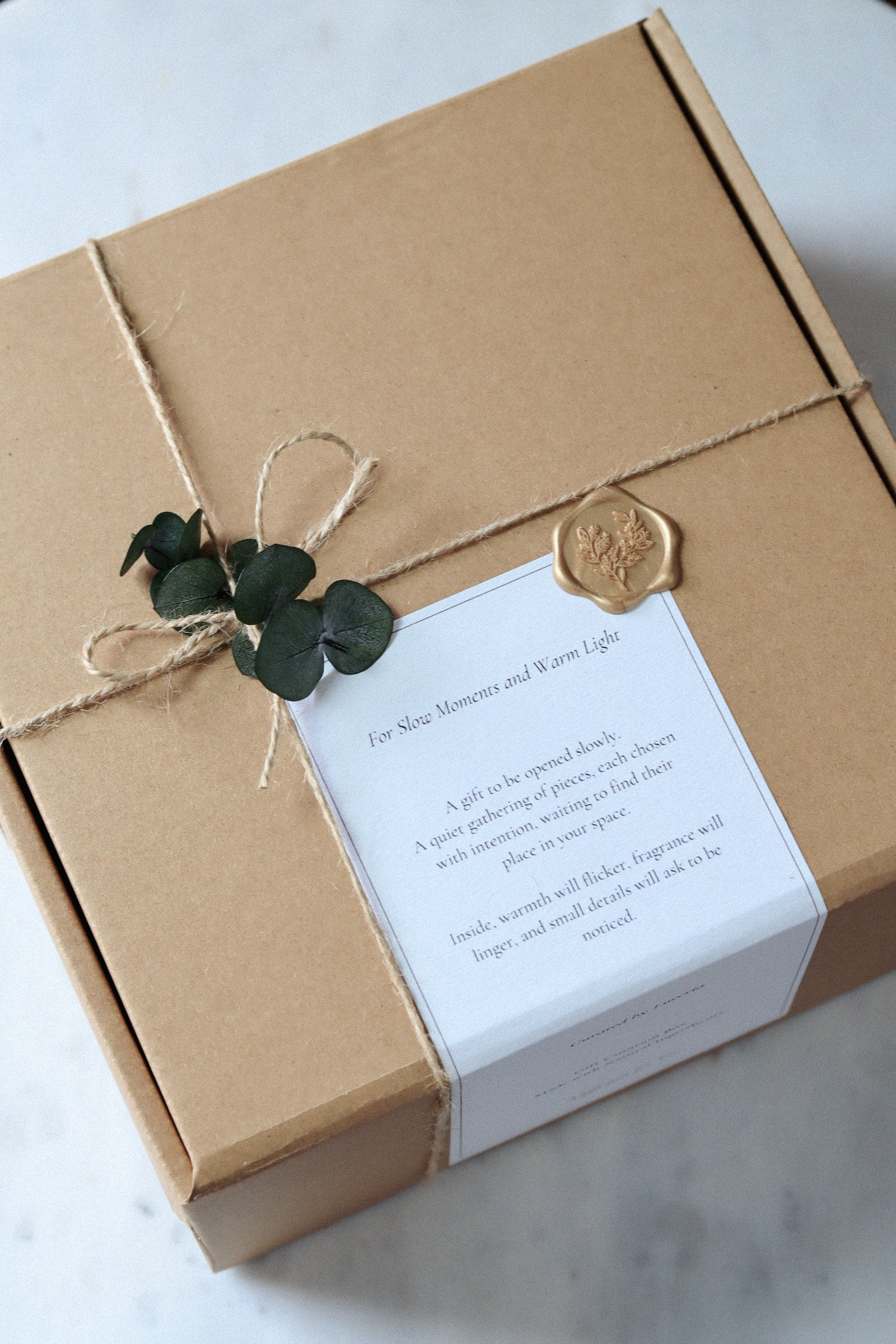 Gift box wrapped in brown paper with a white card and greenery on a light background