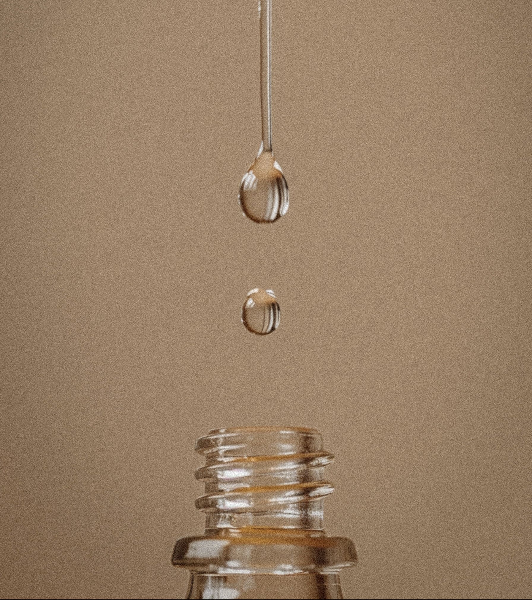 Glass bottle with a droplet of water dripping from a syringe onto a brown background