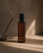 Ember Palo Santo + Sandalwood room and linen spray by Luceria beside smoking incense on a textured beige surface with warm natural light.