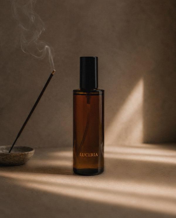 Ember Palo Santo + Sandalwood room and linen spray by Luceria beside smoking incense on a textured beige surface with warm natural light.