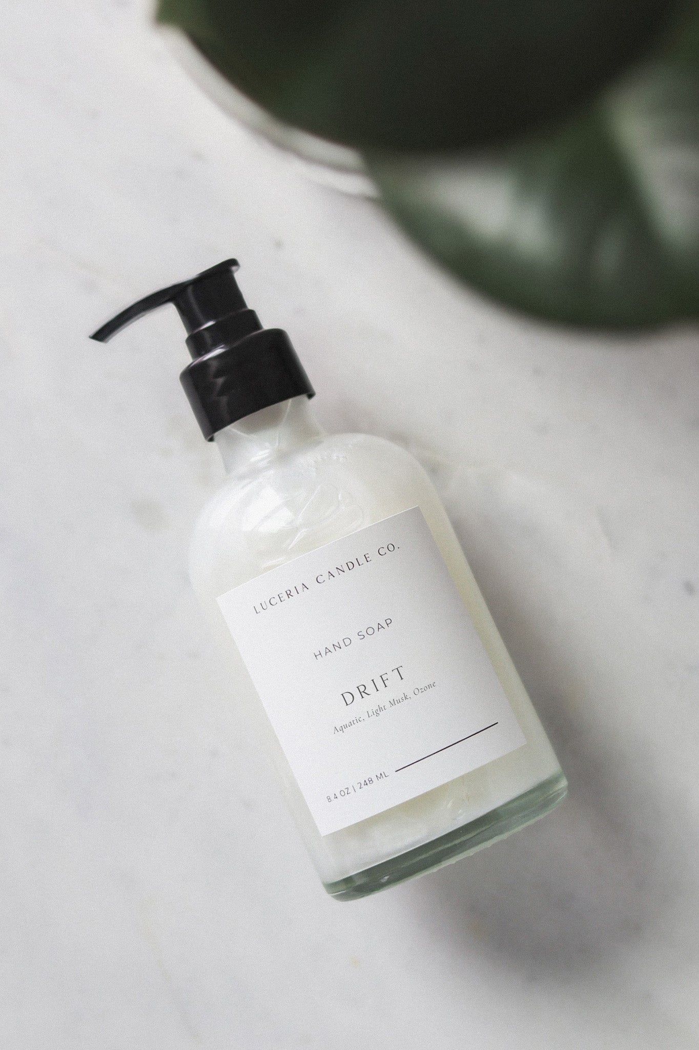 Hand soap bottle labeled 'Drift' on a marble surface with a plant in the background