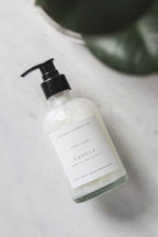 Hand soap bottle labeled 'Vanilla' on a marble surface with a plant in the background