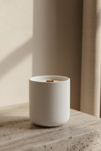 White candle in a ceramic holder on a wooden surface with a neutral background