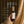 A hand in a beige knit sweater holds a bottle of Luceria Lavender Cedar Room + Linen Spray against a dark brown background with draped beige fabric. White text on the image lists product features and scent details.