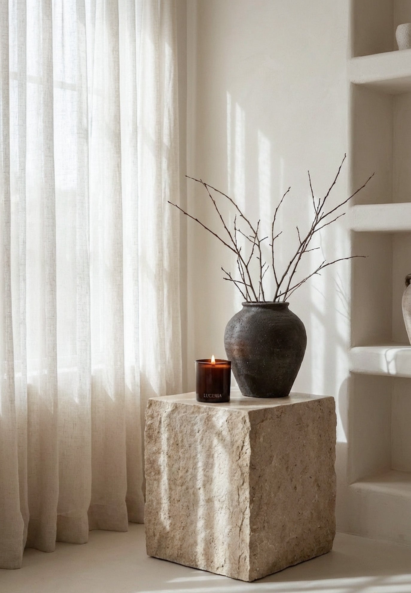 Decorative stone pedestal with a vase and branches against a neutral curtain backdrop