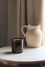 Candle with 'Luceria' branding on a marble surface next to a ceramic vase.