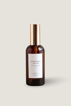 A bottle of Luceria Persimmon and Peach room and linen spray in an amber glass bottle with a gold cap and a white label, set against a solid light beige background.