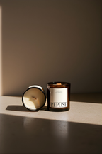 Two candles, one lit and one unlit, on a reflective surface with a neutral background.