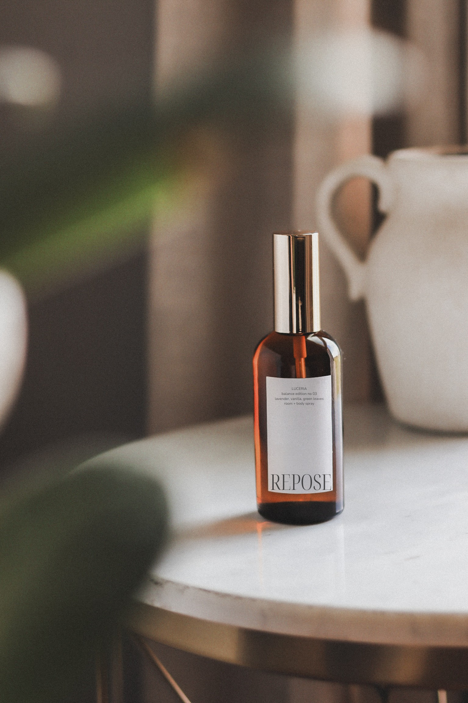 Brown spray bottle labeled 'repose' by Luceria on marble table with textured vase and greenery.