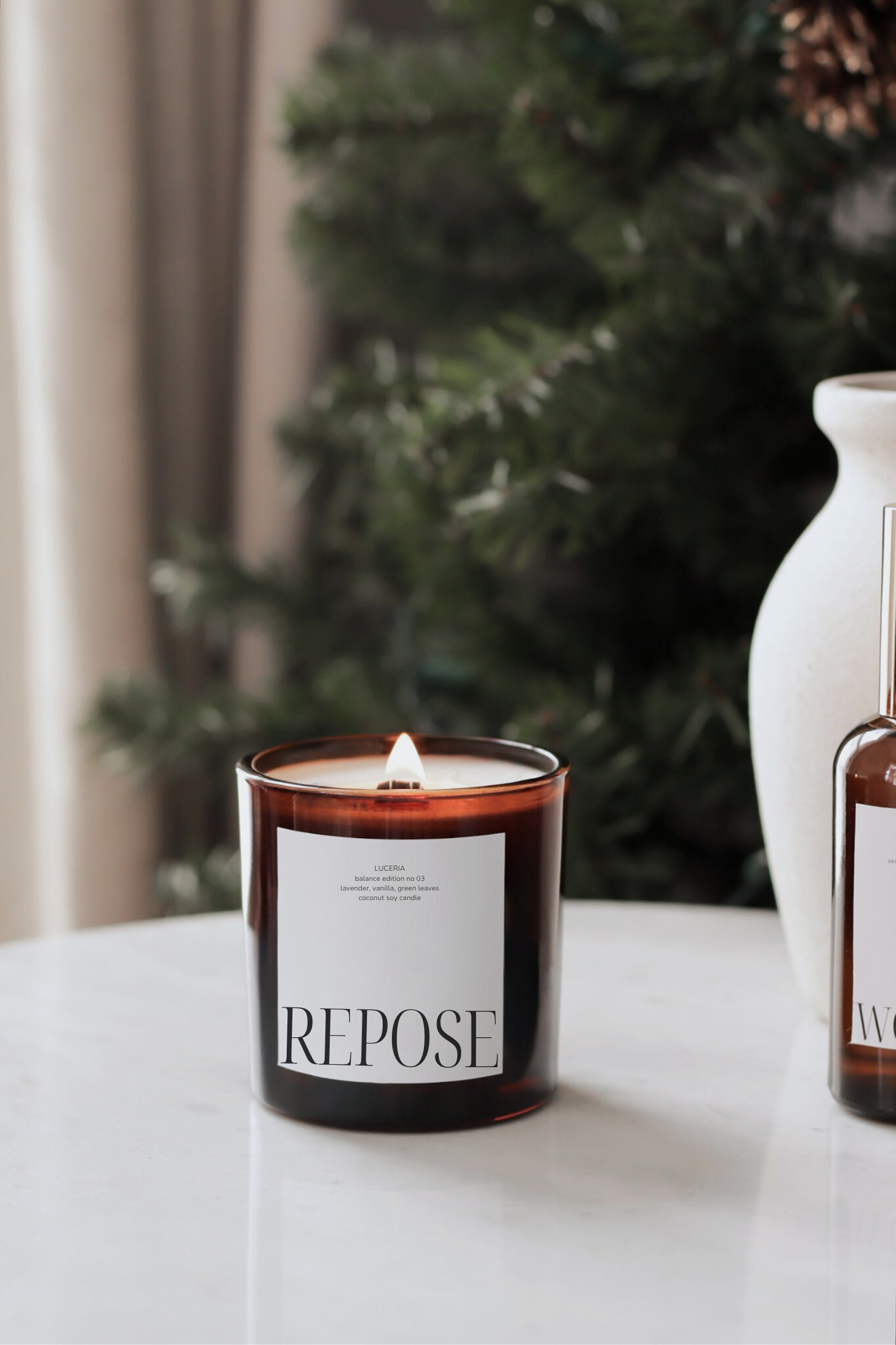 Lavender vanilla scented candle labeled 'Repose' on a table with a Christmas tree in the background