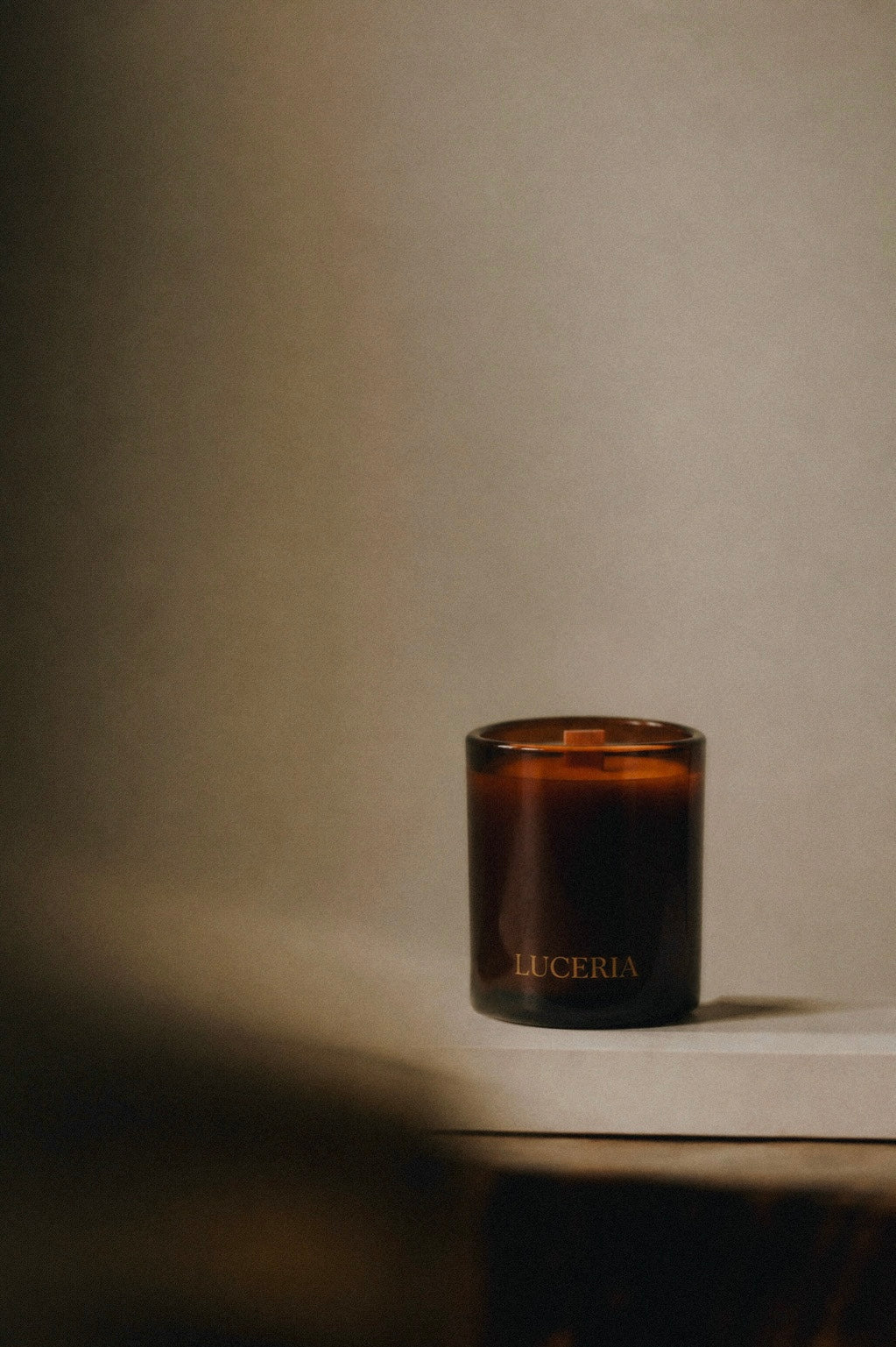 Dark amber glass candle with 'LUCERIA' branding on a neutral background