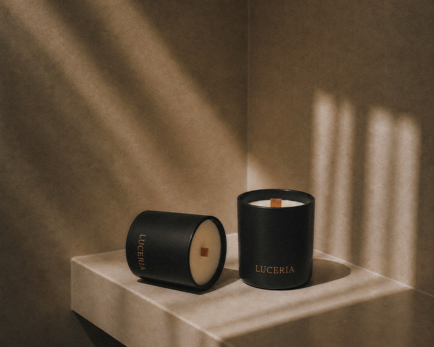 Two black matte soy candles with LUCERIA branding on neutral textured background.