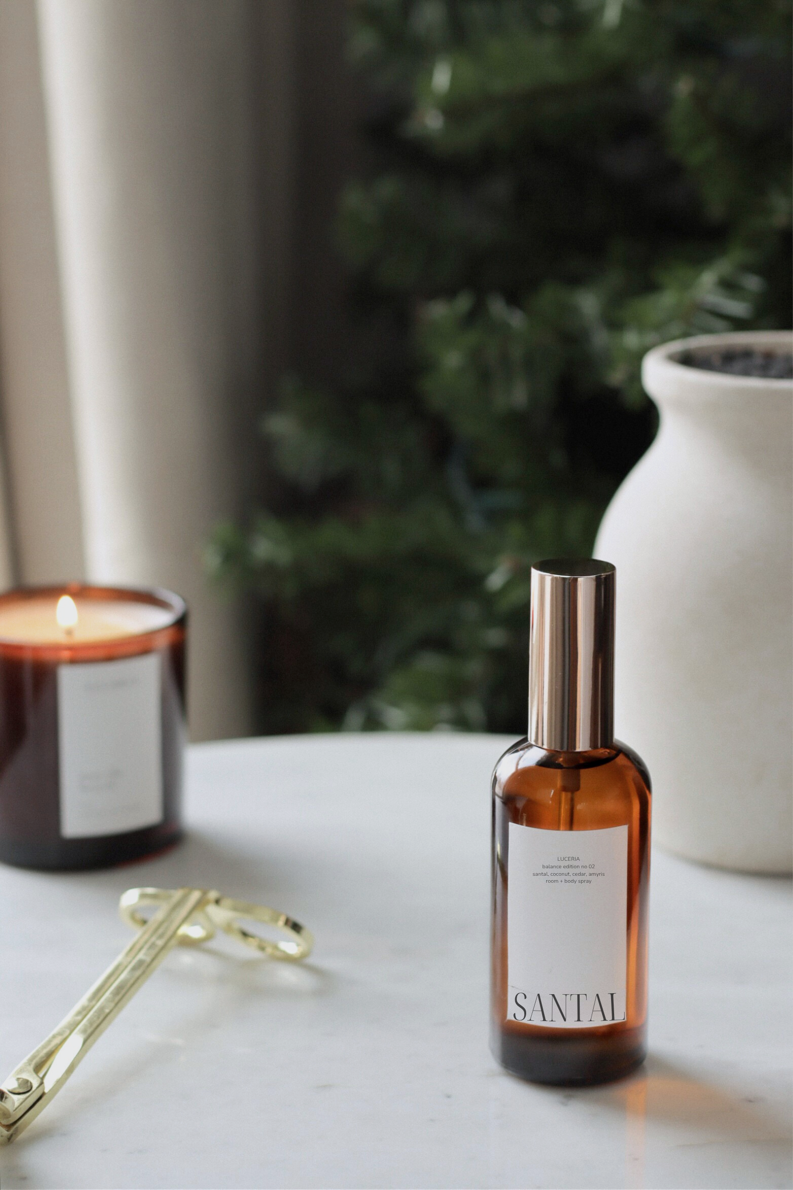 Santal perfume bottle on a marble surface with a candle and decorative items in the background.