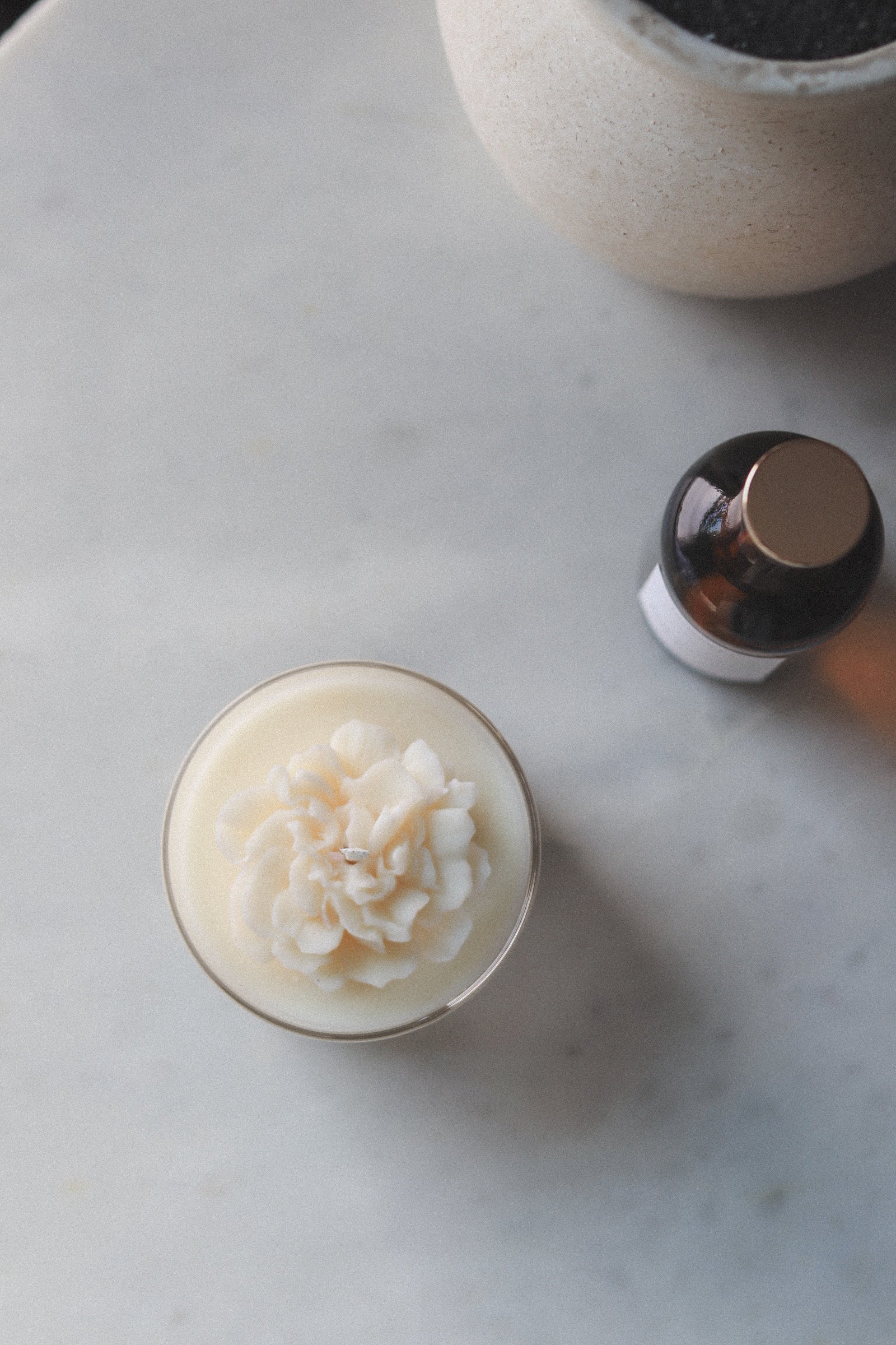 Small candle with floral design on a marble surface next to a bottle.