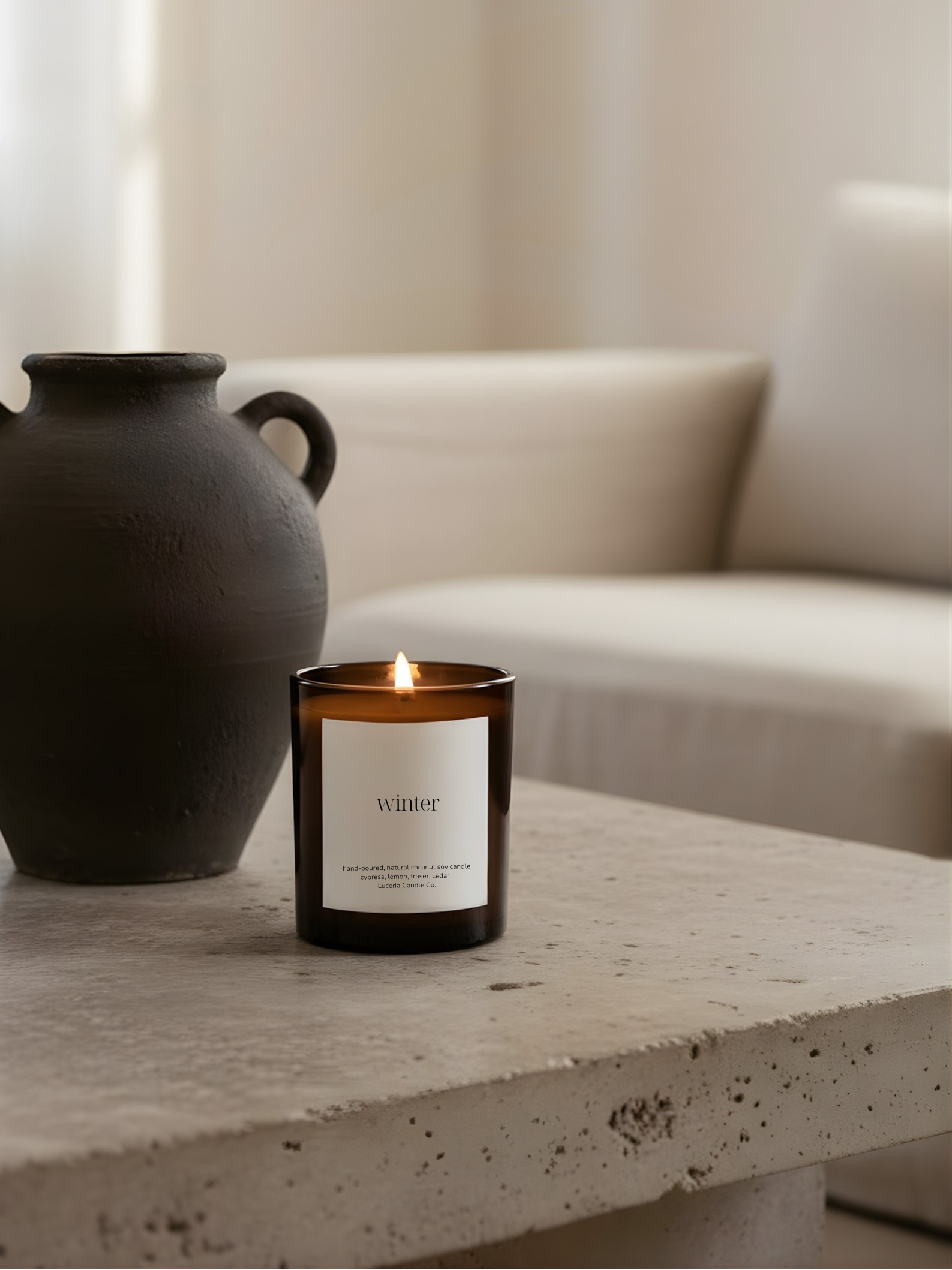 Candle with a label on a stone surface next to a black vase, with a neutral background
